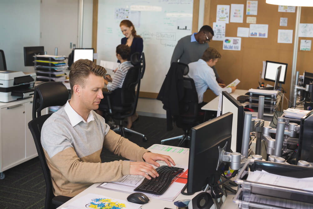 Businessman typing on keyboard while colleagues working in background at office.