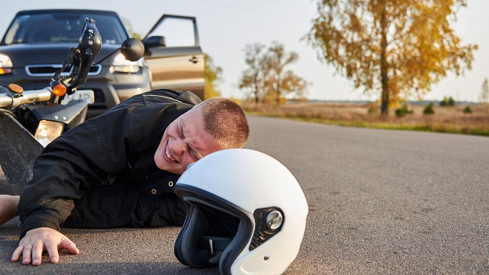 Injured motorcyclist lies on the asphalt near a motorcycle and car after accident.