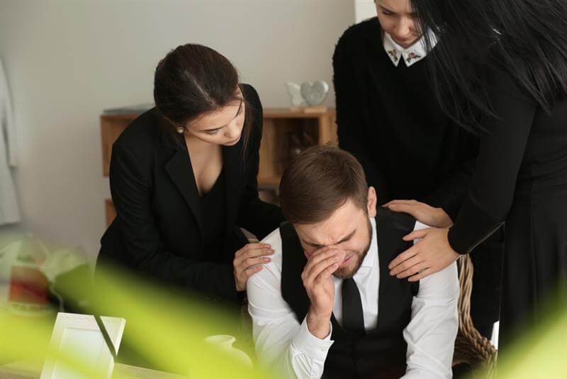 Relatives calming young widower at funeral.